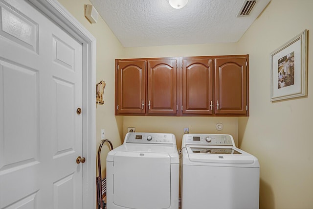 washroom featuring washing machine and dryer, cabinet space, visible vents, and a textured ceiling