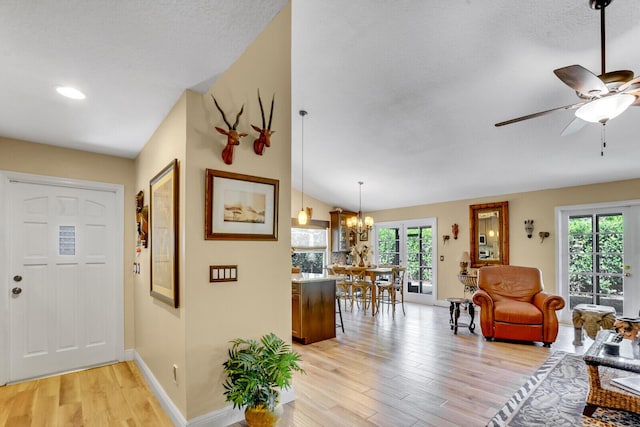 living area featuring ceiling fan with notable chandelier, vaulted ceiling, baseboards, and light wood-style floors