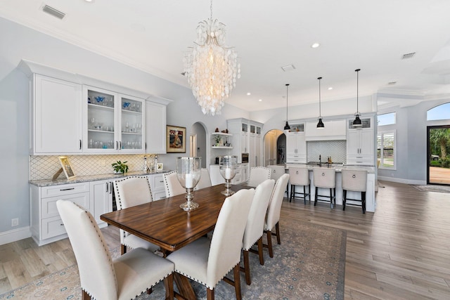 dining room featuring arched walkways, visible vents, light wood-style flooring, and an inviting chandelier