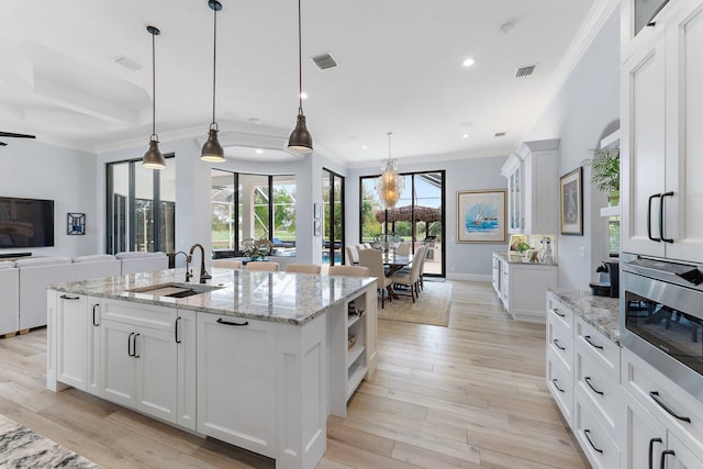 kitchen featuring visible vents, light wood finished floors, a sink, crown molding, and open floor plan