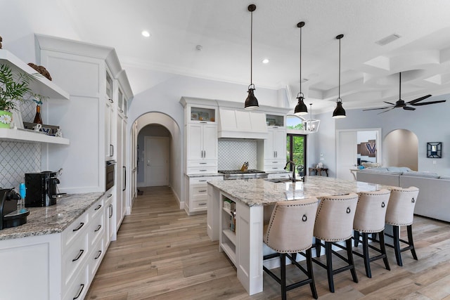 kitchen featuring open shelves, arched walkways, light wood-style flooring, and a sink