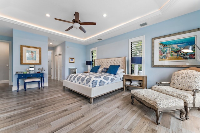 bedroom featuring a tray ceiling, baseboards, light wood-type flooring, and visible vents