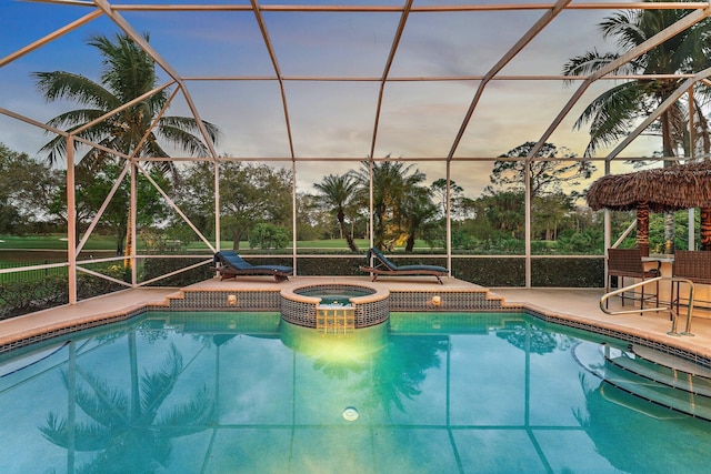 pool at dusk with glass enclosure, a patio, and a pool with connected hot tub