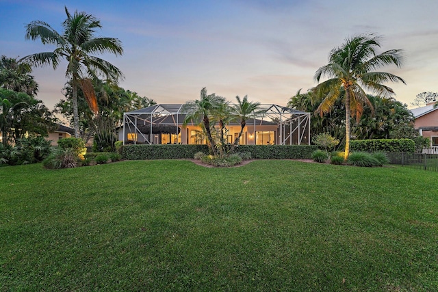 yard at dusk featuring a lanai and fence