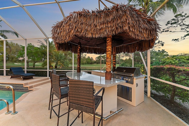 patio terrace at dusk with area for grilling, outdoor dry bar, grilling area, an outdoor pool, and a lanai