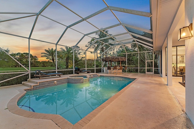 pool at dusk featuring a lanai, a pool with connected hot tub, and a patio