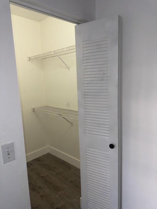 walk in closet with dark wood-style floors