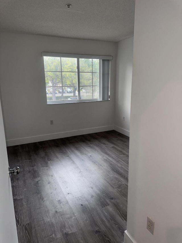 spare room with baseboards, dark wood finished floors, and a textured ceiling