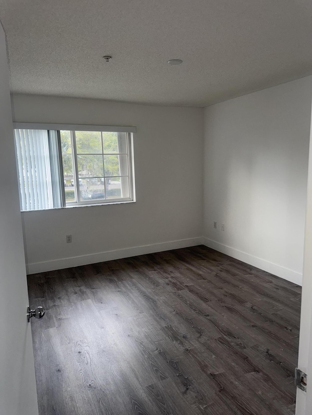 spare room with baseboards, dark wood finished floors, and a textured ceiling