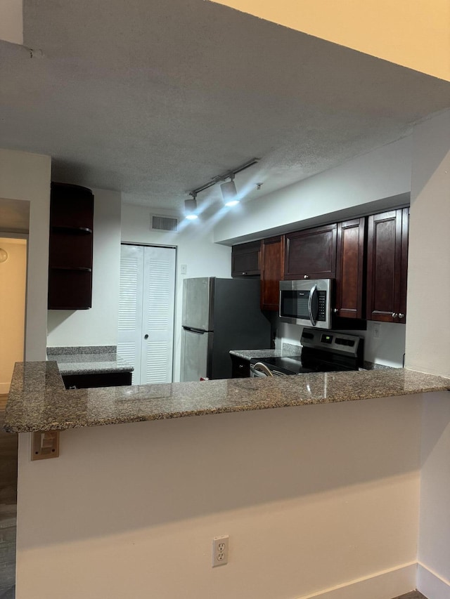 kitchen featuring stainless steel appliances, visible vents, a textured ceiling, dark brown cabinets, and dark stone countertops