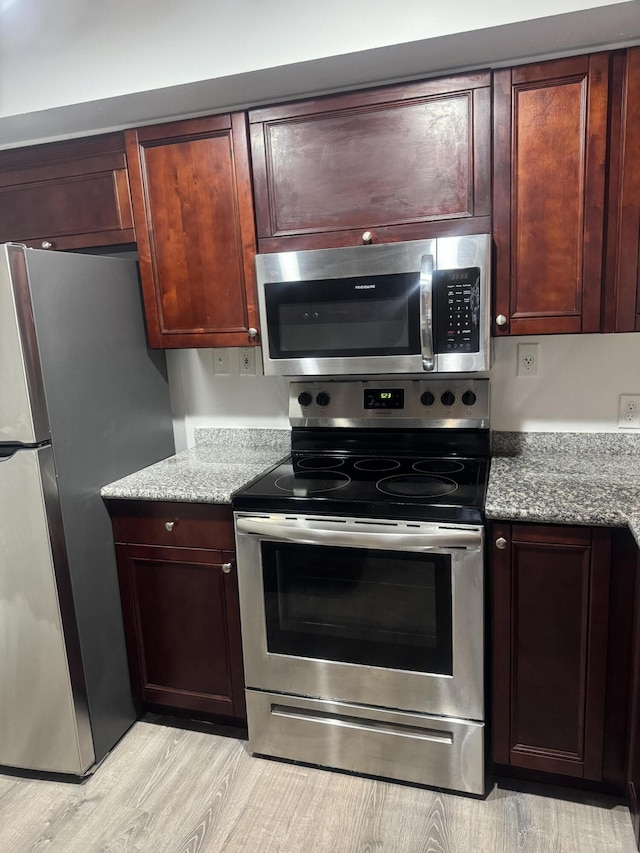 kitchen featuring appliances with stainless steel finishes, light stone counters, and light wood finished floors