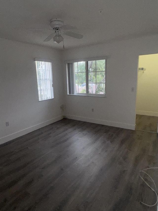 empty room with a ceiling fan, a wealth of natural light, dark wood-style flooring, and baseboards