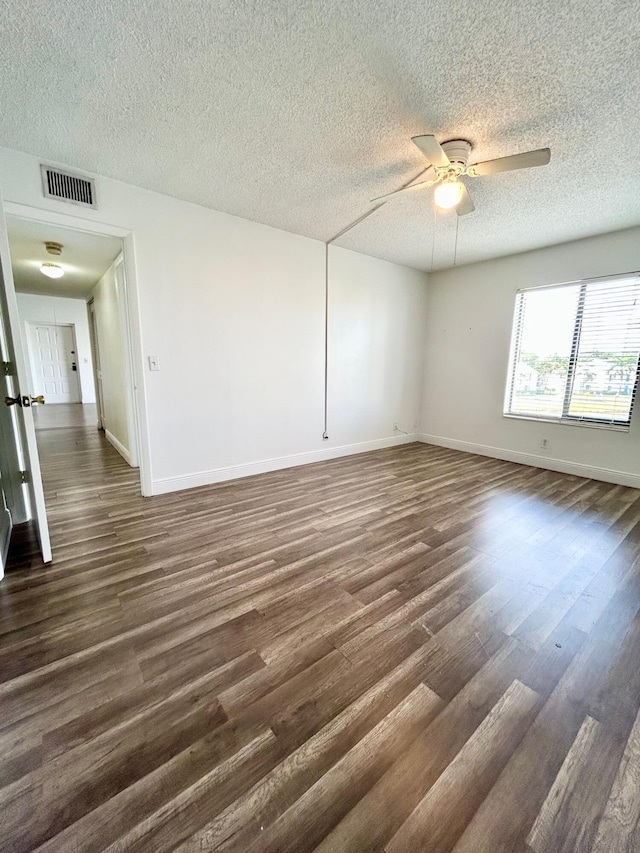 empty room with a textured ceiling, dark wood-style flooring, visible vents, baseboards, and a ceiling fan