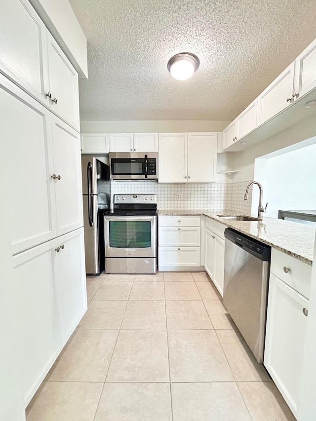 kitchen with stainless steel appliances, light tile patterned flooring, a sink, and white cabinetry