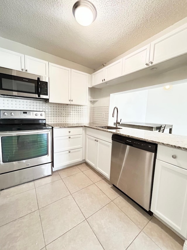 kitchen featuring light stone counters, light tile patterned flooring, stainless steel appliances, a sink, and white cabinetry