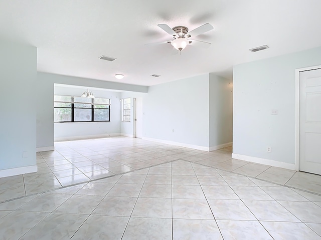 spare room with light tile patterned flooring, visible vents, ceiling fan with notable chandelier, and baseboards