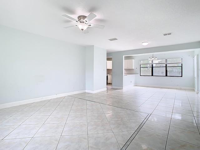 empty room with light tile patterned floors, visible vents, ceiling fan with notable chandelier, and baseboards