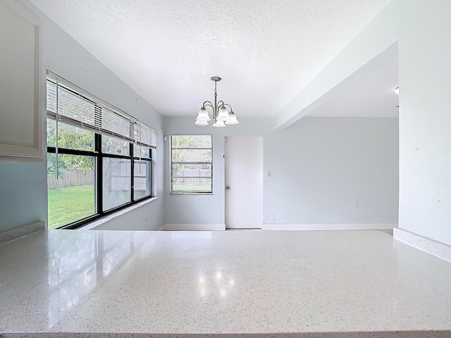 unfurnished room with beam ceiling, a notable chandelier, a textured ceiling, and baseboards