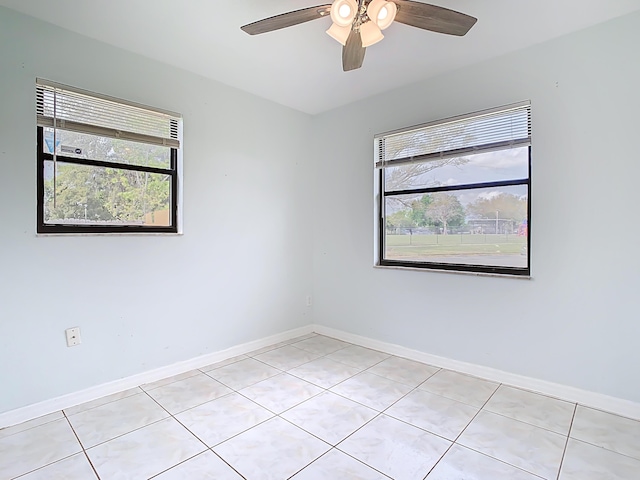 spare room featuring a ceiling fan, light tile patterned flooring, a healthy amount of sunlight, and baseboards