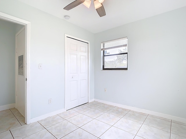 unfurnished bedroom featuring light tile patterned floors, a closet, baseboards, and a ceiling fan