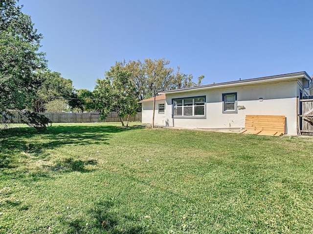 back of property with stucco siding, a yard, and fence