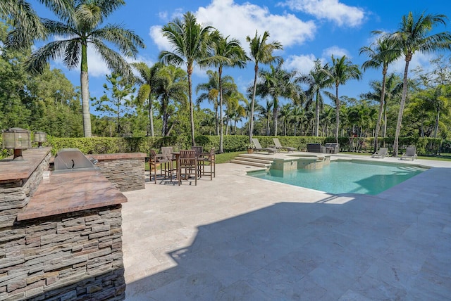 view of pool with a patio, a pool with connected hot tub, a grill, fence, and exterior kitchen