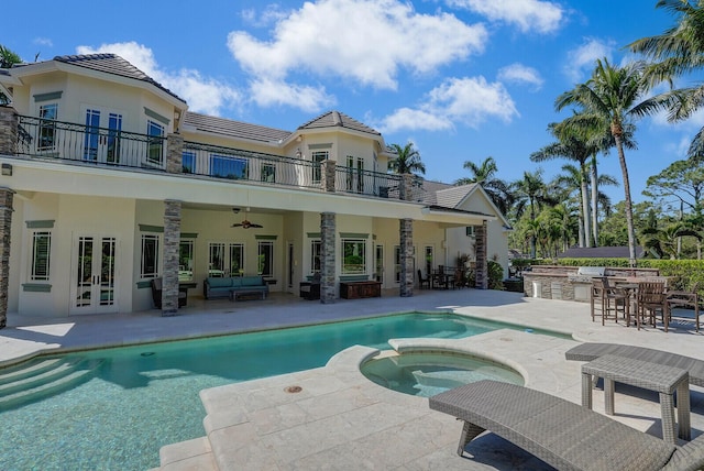 rear view of property with a balcony, outdoor dry bar, french doors, a patio area, and stucco siding