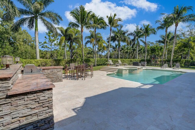 view of pool with a patio area, grilling area, fence, exterior kitchen, and a pool with connected hot tub
