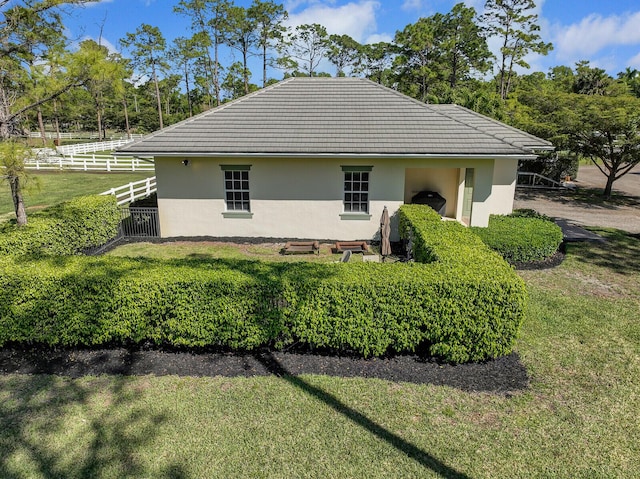 view of side of property with stucco siding, a yard, a tiled roof, and fence