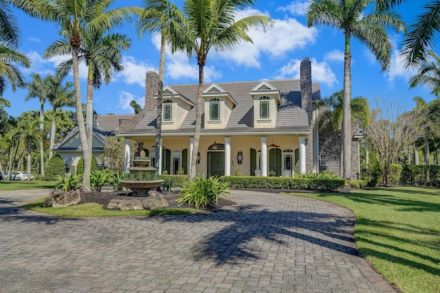 cape cod home with covered porch, a front yard, a chimney, and stucco siding