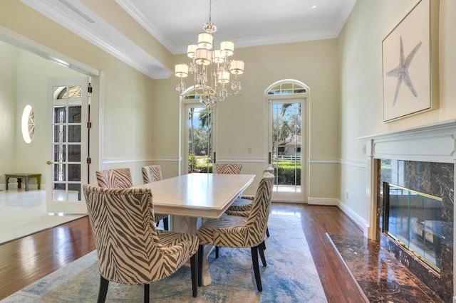 dining space with ornamental molding, a high end fireplace, a chandelier, baseboards, and hardwood / wood-style flooring