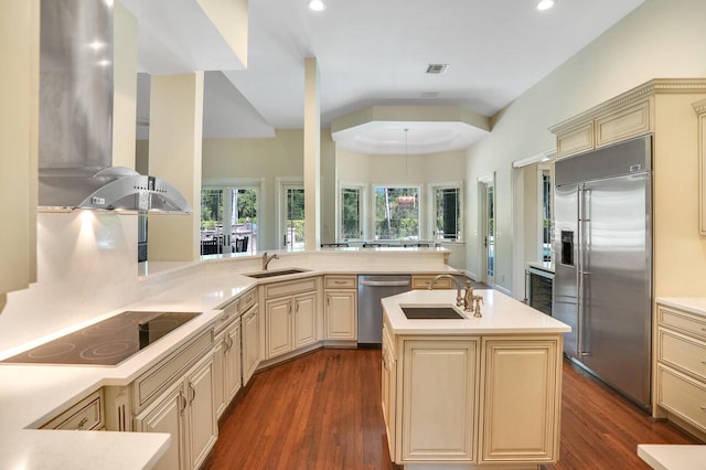 kitchen featuring a peninsula, cream cabinets, stainless steel appliances, wall chimney range hood, and a sink