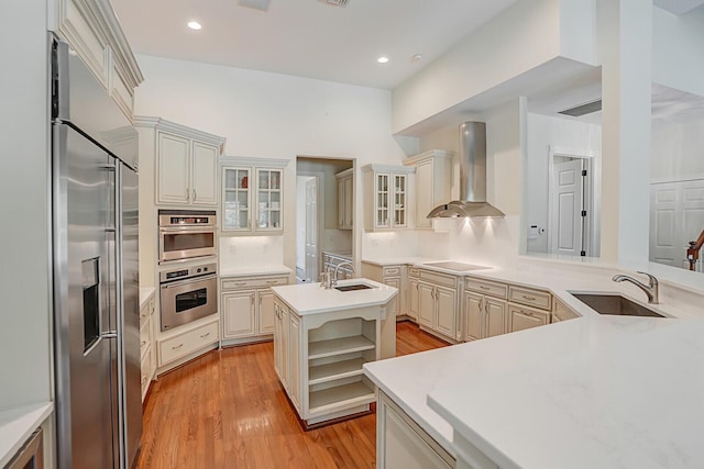 kitchen with a sink, light wood-style floors, appliances with stainless steel finishes, wall chimney range hood, and open shelves