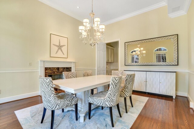 dining room with wood finished floors, a fireplace, a notable chandelier, and ornamental molding