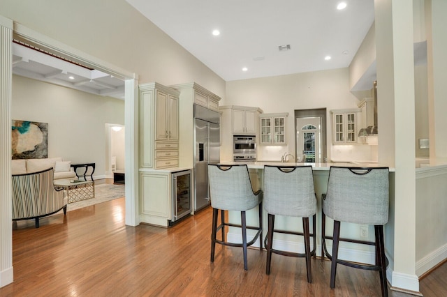 kitchen featuring beverage cooler, a breakfast bar area, wood finished floors, a peninsula, and stainless steel appliances