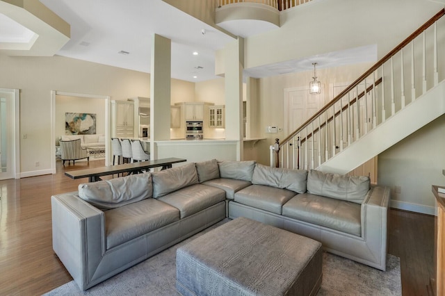 living area with recessed lighting, wood finished floors, a towering ceiling, baseboards, and stairway