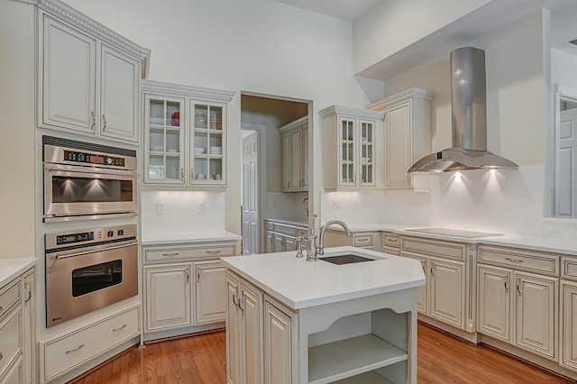 kitchen with ventilation hood, a sink, light wood-style floors, stainless steel double oven, and light countertops
