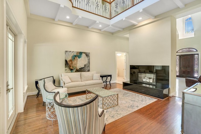 living area featuring wood finished floors, a fireplace with raised hearth, a towering ceiling, and beam ceiling