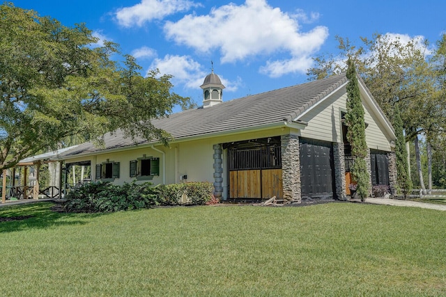 view of side of property featuring a yard, stone siding, an attached garage, and a tile roof