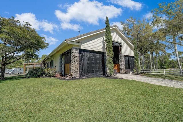 view of home's exterior featuring driveway, stone siding, fence, a garage, and a lawn
