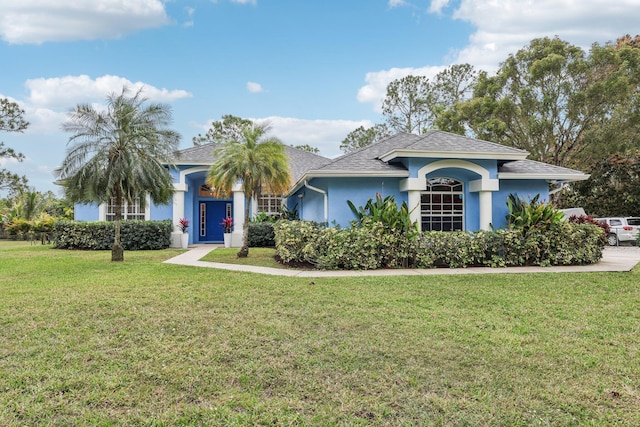 view of front of home with a shingled roof, a front yard, and stucco siding