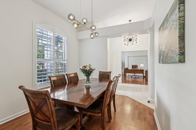 dining room with a notable chandelier, baseboards, wood finished floors, and ornate columns