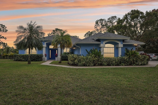 view of front facade featuring a shingled roof, a lawn, and stucco siding