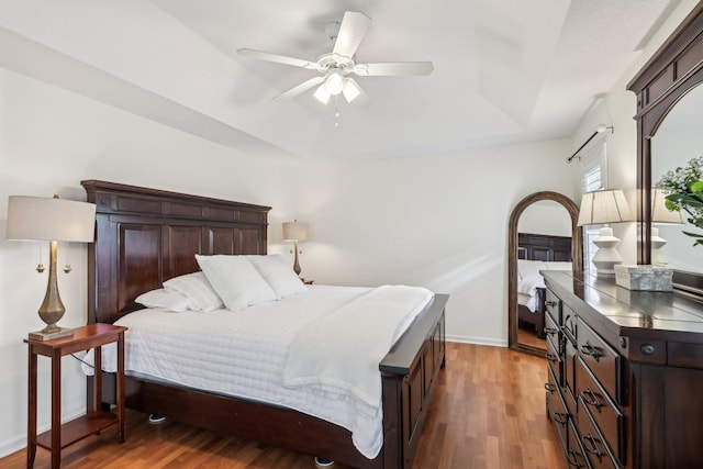 bedroom with baseboards, ceiling fan, a tray ceiling, and wood finished floors