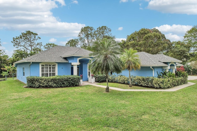 ranch-style home featuring a shingled roof, a front yard, and stucco siding