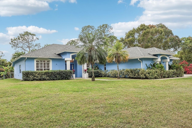 ranch-style home with roof with shingles, a front lawn, and stucco siding