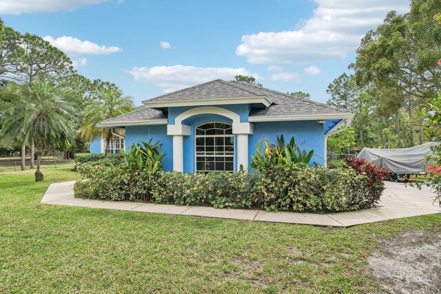 exterior space with a shingled roof, a lawn, fence, and stucco siding