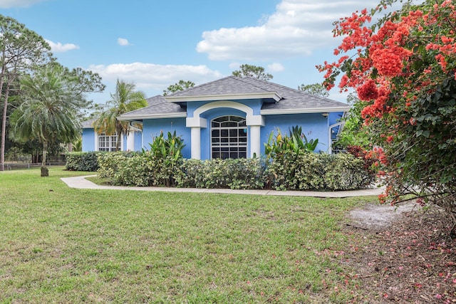 ranch-style house with roof with shingles, a front lawn, and stucco siding