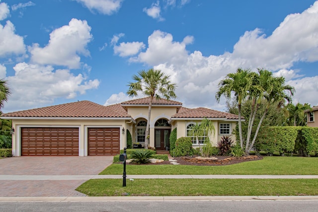 mediterranean / spanish-style house featuring a tile roof, an attached garage, decorative driveway, a front lawn, and stucco siding