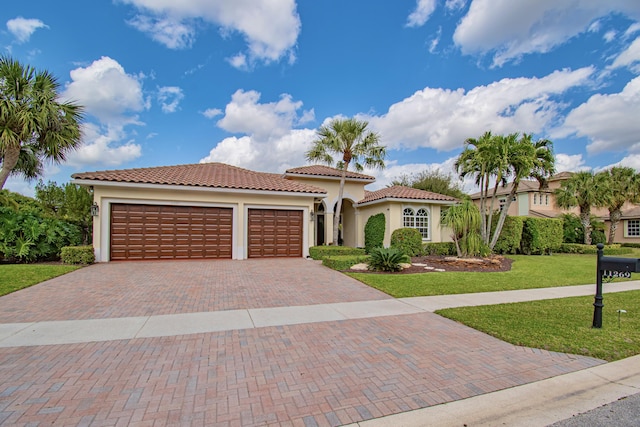 mediterranean / spanish home with decorative driveway, a tile roof, stucco siding, a garage, and a front lawn